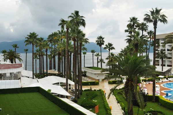 Yeşil park, palmiye ağaçları, havuz ve bulutlar dağlar ile deniz ile Otel