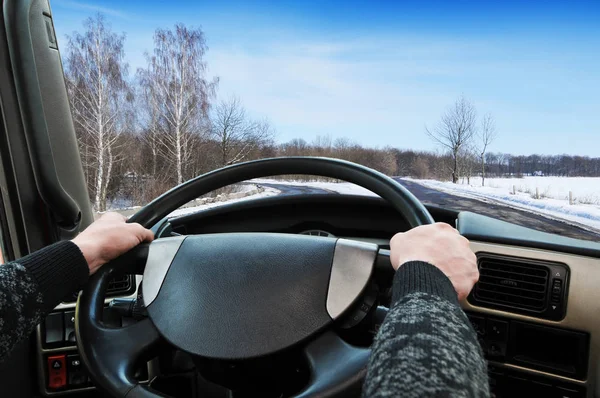 Truck dashboard with driver hands on steering wheel on winter road with white snow and blue sky