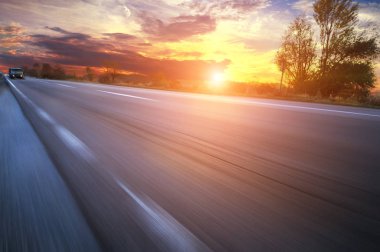 Parlak gün batımı ile akşam gökyüzüne karşı kamyon ve araba ile hareket asfalt kırsal yol
