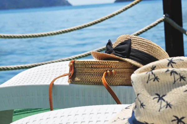 Arka planda deniz ile iskelede plastik şezlong üzerinde Yuvarlak hasır çanta ve hasır şapka