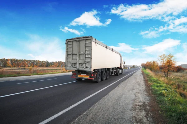 Big truck with white trailer on countryside road against blue sky with clouds