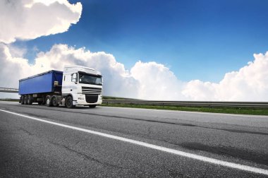 Kırsal yolda mavi karavanlı büyük beyaz kamyon Bulutlu mavi gökyüzüne karşı