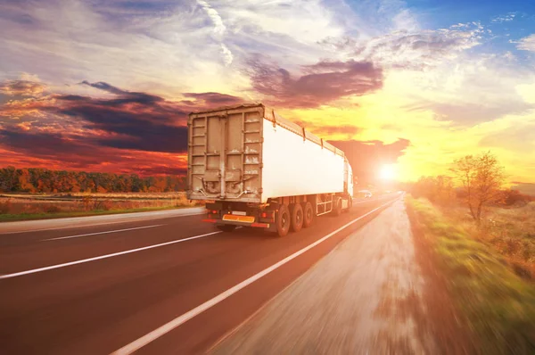 日没と空に対する田舎道上の動きで白いトレーラーを持つ大きなトラック — ストック写真