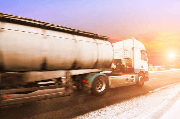 White big metal fuel tanker truck shipping fuel on the winter countryside road with snow against sky with sunset