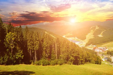 Yeşil ormanlı Karpat Dağları, kayak merkezi binaları ve yazın günbatımında gökyüzü