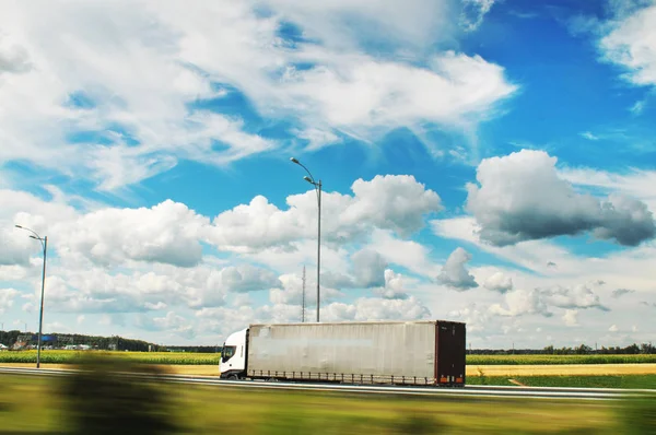 青い空と雲とフィールドと緑の木と運動中の田舎道上のトレーラー付きの青いトラック — ストック写真
