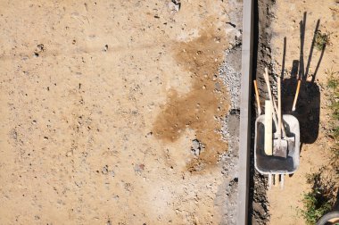 Arka planda kum, taş ve çimen olan eski metal el arabası ve küreklerin üst görüntüsü