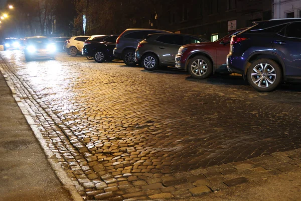 Stadtpflasterstraße Mit Geparkten Autos Und Leuchtend Orangefarbenen Lichtern Der Nacht lizenzfreie Stockfotos