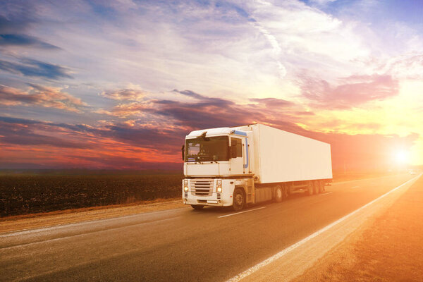 Big white truck and trailer with space for text on the countryside road against sky with sunset