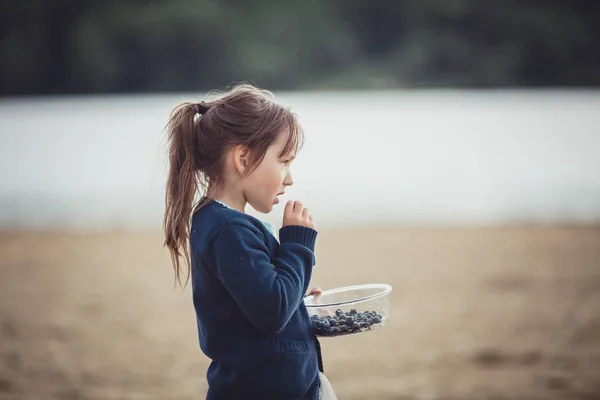 Het eten van bosbessen uit een glazen kom meisje — Stockfoto