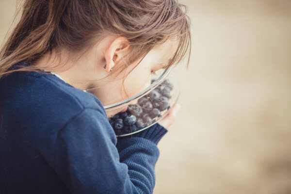 The girl eating blueberries from a glass bowl 