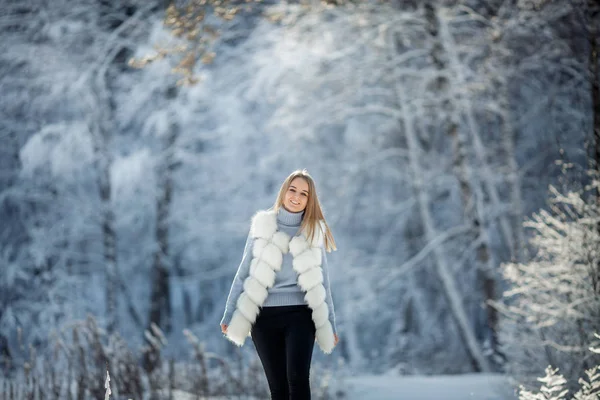 Outdoor portrait of beautiful young woman in snowy forest at sunny frozen day