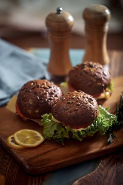 Karanlık burger tahıl ekmeği koyu seramik tabak, salata, biberiye ve limon ile 