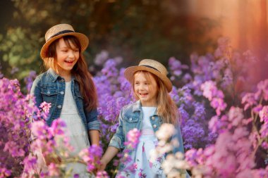 Pembe bir çayırda küçük kız kardeşler açık hava portresi 