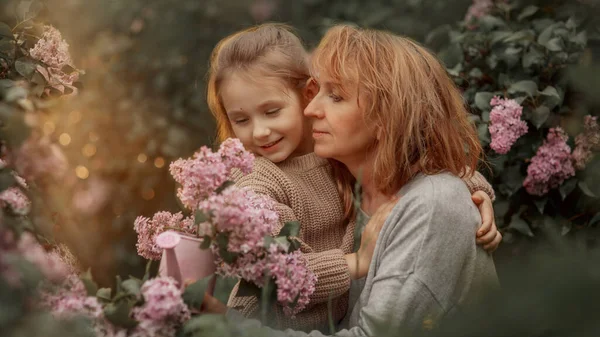 Sorrindo Abraços Menina Com Sua Avó Jardim Lilás Primavera — Fotografia de Stock
