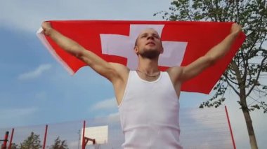 Gökyüzüne iki elle İsviçre Ulusal bayrak tutan genç adam