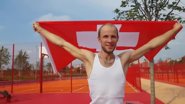 Joven sosteniendo bandera nacional suiza en el cielo con dos manos — Vídeo de stock