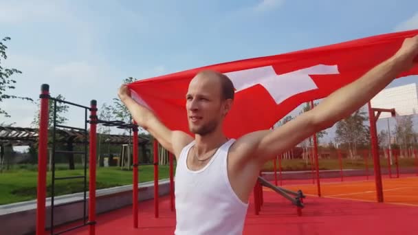 Молодой человек держит швейцарский национальный флаг на небе двумя руками — стоковое видео
