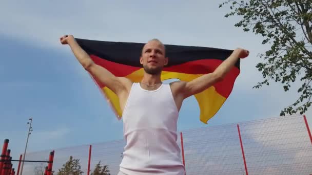 Молодой человек держит немецкий национальный флаг на небе двумя руками — стоковое видео