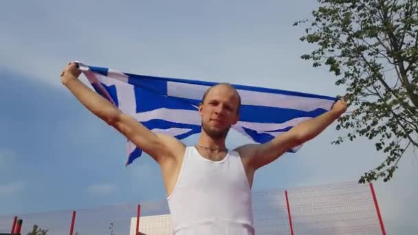 Junger Mann hält griechische Nationalflagge mit zwei Händen in den Himmel — Stockvideo
