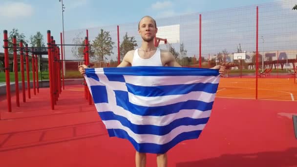 junger Mann hält griechische Nationalflagge mit zwei Händen in den Himmel