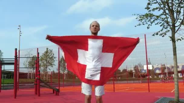 Junger Mann hält Schweizer Nationalflagge mit zwei Händen in den Himmel — Stockvideo