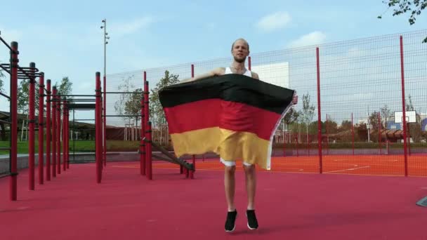 Молодой человек держит немецкий национальный флаг на небе двумя руками — стоковое видео