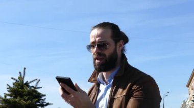 Sakallı işadamı saldırgan bir şekilde cep telefonuyla iletişim kuruyor.