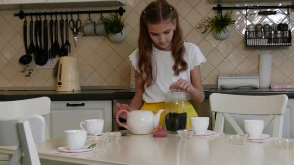 Ένα κορίτσι καθαρίζει ένα σερβίτσιο τσαγιού από το τραπέζι της κουζίνας — Αρχείο Βίντεο