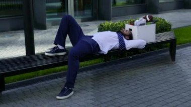 Bir adam ofiste şeyler ile bir kutunun yanında bir bankta yatıyor.