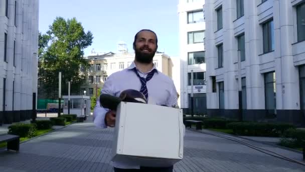positiver Mann läuft mit einer Schachtel mit Sachen aus dem Büro die Straße hinunter.