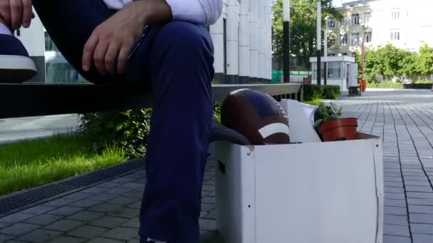 Коробка с вещами уволенного сотрудника на скамейке рядом с его владельцем — стоковое видео