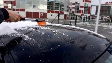 Adam arabayı kardan temizliyor.