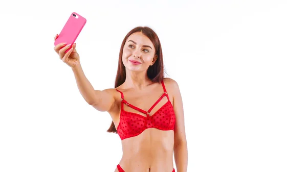 Sexy donna in rosso biancheria intima making selfie utilizzando smartphone e sorridente — Foto Stock