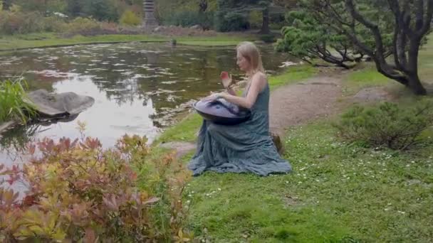 Popular, modern hang musical instrument in the hands of a beautiful blonde in park. — Stock Video