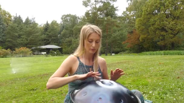 Popular, modern hang musical instrument in the hands of a beautiful blonde in park. — Stock Video