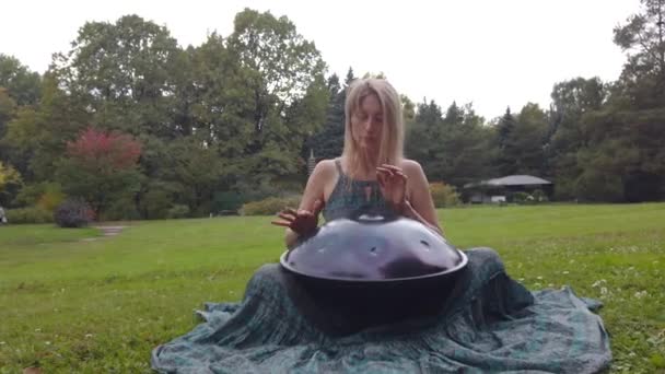 Popular, modern hang musical instrument in the hands of a beautiful blonde in park. — Stock Video