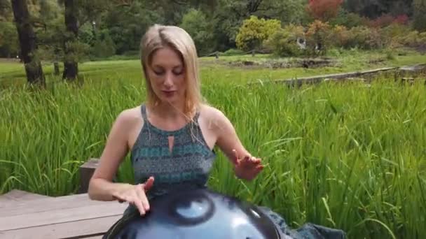 Popular, modern hang musical instrument in the hands of a beautiful blonde in park. — Stock Video