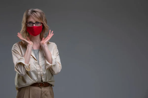 Jeune femme blonde en masque de protection rouge à la mode contre les virus, tient sa tête. — Photo