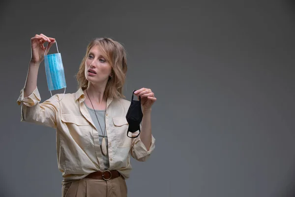 Retrato de la cabeza atractiva mujer rubia haciendo difícil elección entre la máscara quirúrgica y el tejido — Foto de Stock