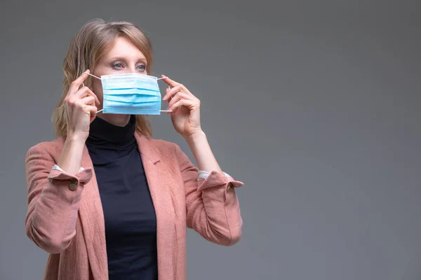 Ξανθιά γυναίκα κρατά τη χειρουργική της μάσκα Εικόνα Αρχείου