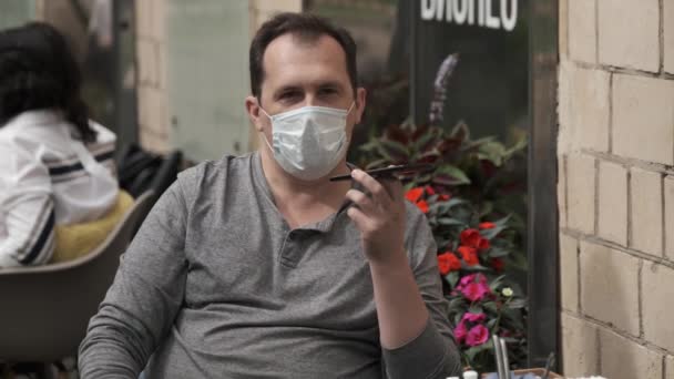 Homem em uma máscara médica falando em um telefone celular usando um mensageiro moderno para comunicação de vídeo — Vídeo de Stock
