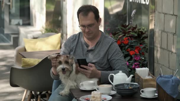 Hombre usando teléfono móvil con perro pequeño acostado en su regazo — Vídeos de Stock