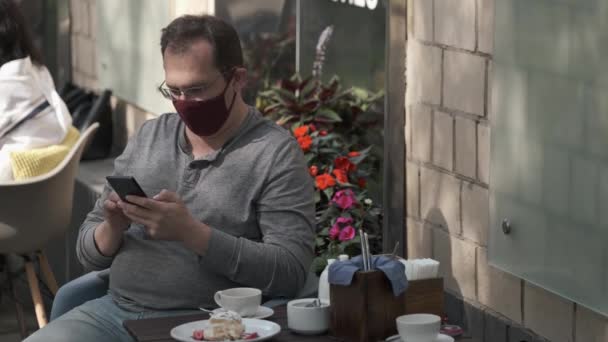 Άντρας με ιατρική μάσκα μιλάει σε κινητό τηλέφωνο χρησιμοποιώντας έναν σύγχρονο αγγελιοφόρο για βιντεοεπικοινωνία — Αρχείο Βίντεο