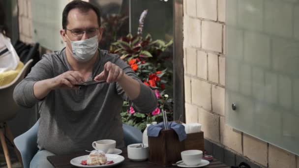 Homem tem couh em máscara médica fazendo foto de comida em um telefone celular durante uma pandemia — Vídeo de Stock