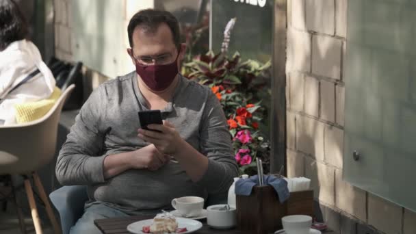 Mann mit medizinischer Maske spricht auf einem Mobiltelefon und benutzt einen modernen Messenger für die Videokommunikation — Stockvideo