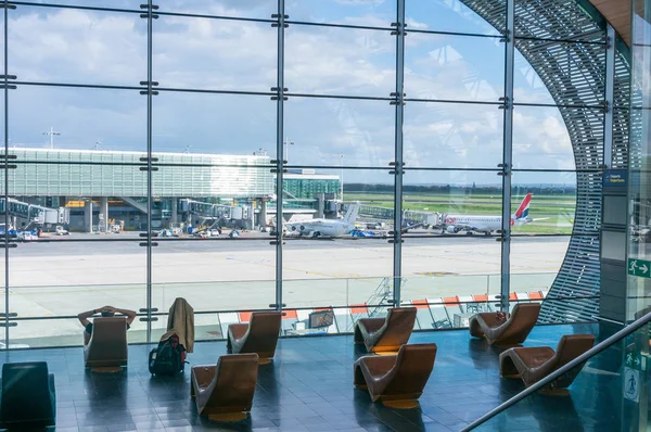 Paris, Frankrike, den 1 April 2017: Tittar ut ett stort ellipsoid fönster på Charles De Gaulle flygplats med två rader med stolar i siluett framför den — Stockfoto