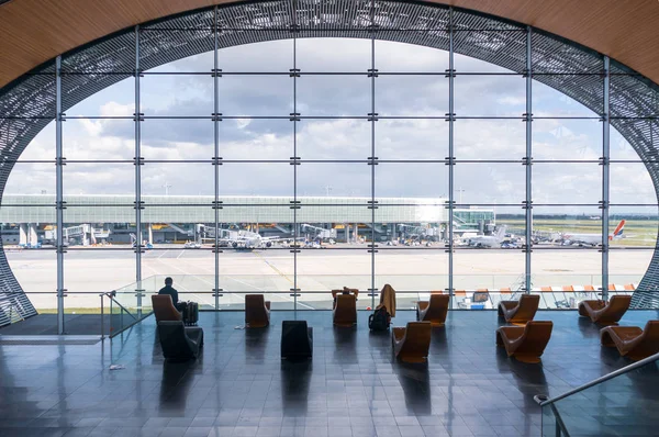 Paris, Frankrike, den 1 April 2017: Tittar ut ett stort ellipsoid fönster på Charles De Gaulle flygplats med två rader med stolar i siluett framför den — Stockfoto