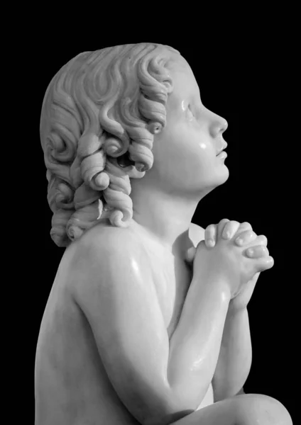 Pojkstatyn ber till Gud med händerna sammanhållna. Vacker gammal sten staty av bedjande barn isolerad på svart bakgrund — Stockfoto