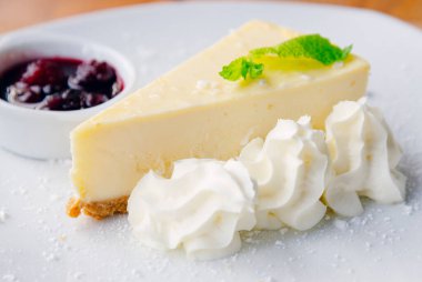 Bir dilim peynirli kek ve beyaz tabakta meyveler.